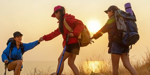 Group Hiker team woman helping her friend climb up the last section of sunset in mountains. Traveler teamwork and family relax walking in outdoor lifestyle adventure and camping. Travel summer life Concept.