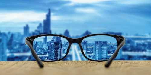 Clear cityscape focused in glasses lenses with blurred cityscape background.