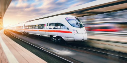 White modern speed train in motion on railway station at sunset. Train on railroad track with motion blur effect in Europe in evening. Railway platform. Industrial landscape. Railway tourism